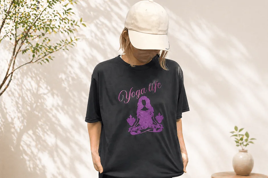 ベージュのキャップと黒いTシャツを着用した人物が写っています。Tシャツには「Yoga life」の文字と瞑想する女性のイラストが紫で描かれています。背景には植物と壁に映る影が見えます。
