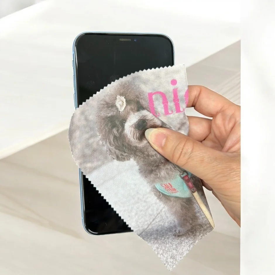 手が水色のスマートフォンの画面を、犬のイラストと「ni」の文字がプリントされたクリーニングクロスで拭いている様子