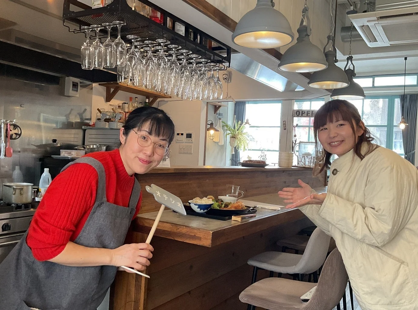 明るい雰囲気のレストランまたはカフェで、二人の女性が笑顔でポーズをとっています。