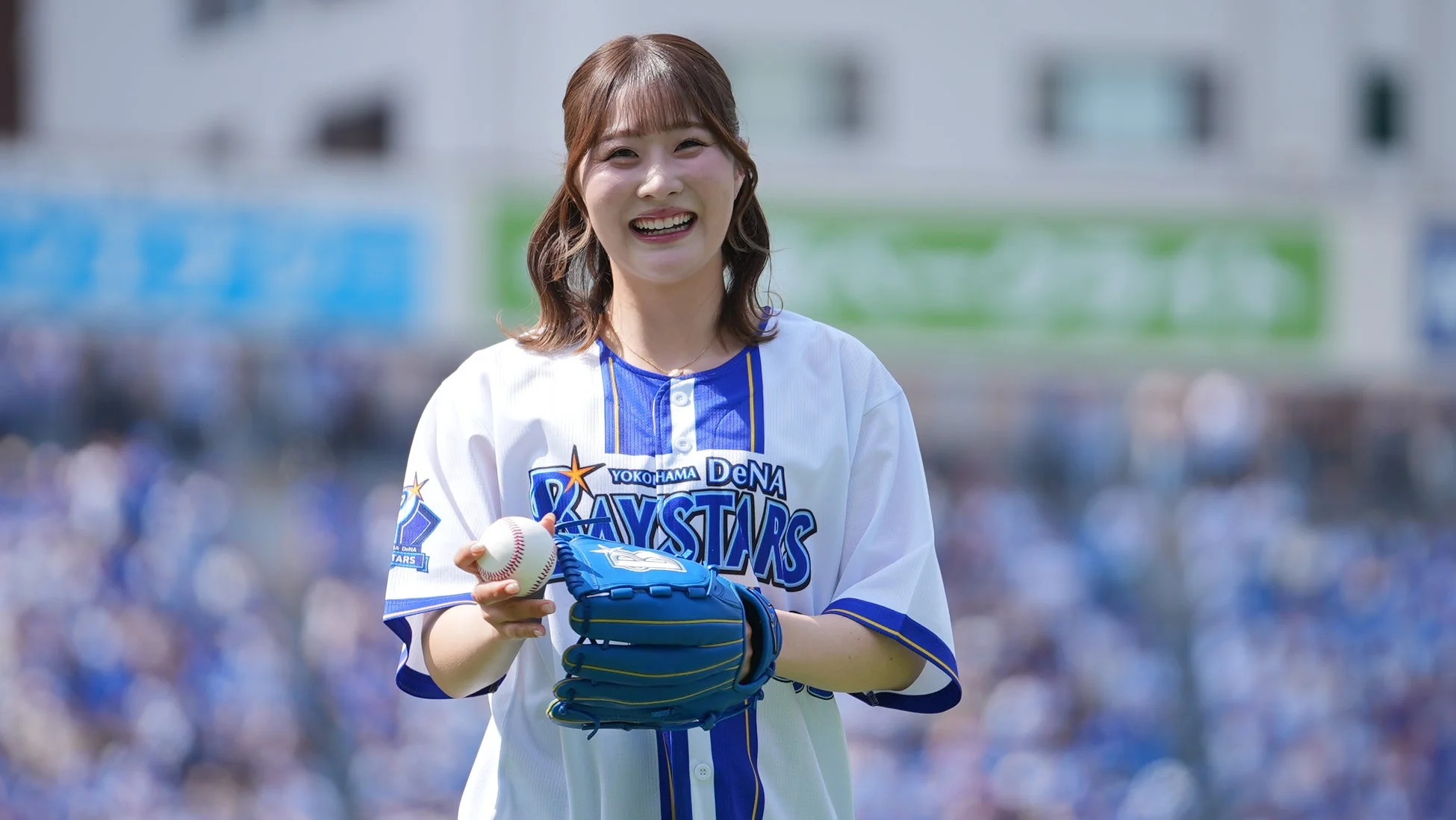 横浜DeNAベイスターズのユニフォームを着た女性が、笑顔で野球のボールとグローブを持っている様子