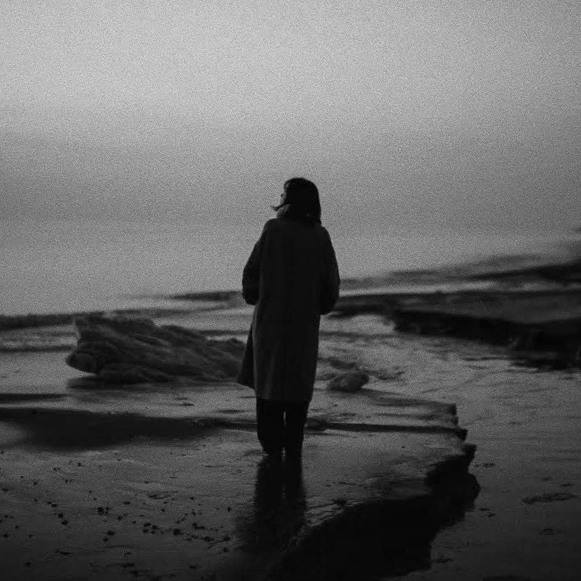 海岸を歩く人物の後ろ姿のモノクロ写真