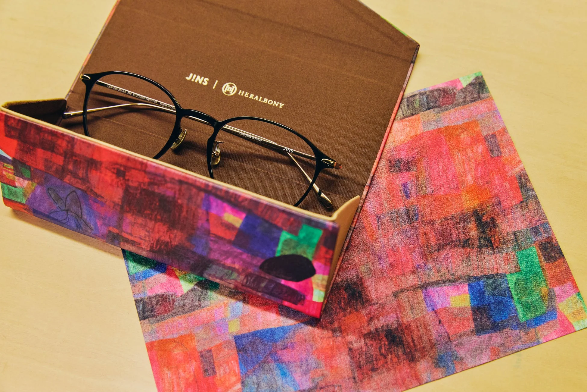 JINSとHERALBONYのコラボレーションによるメガネと、その鮮やかな抽象画デザインのケース