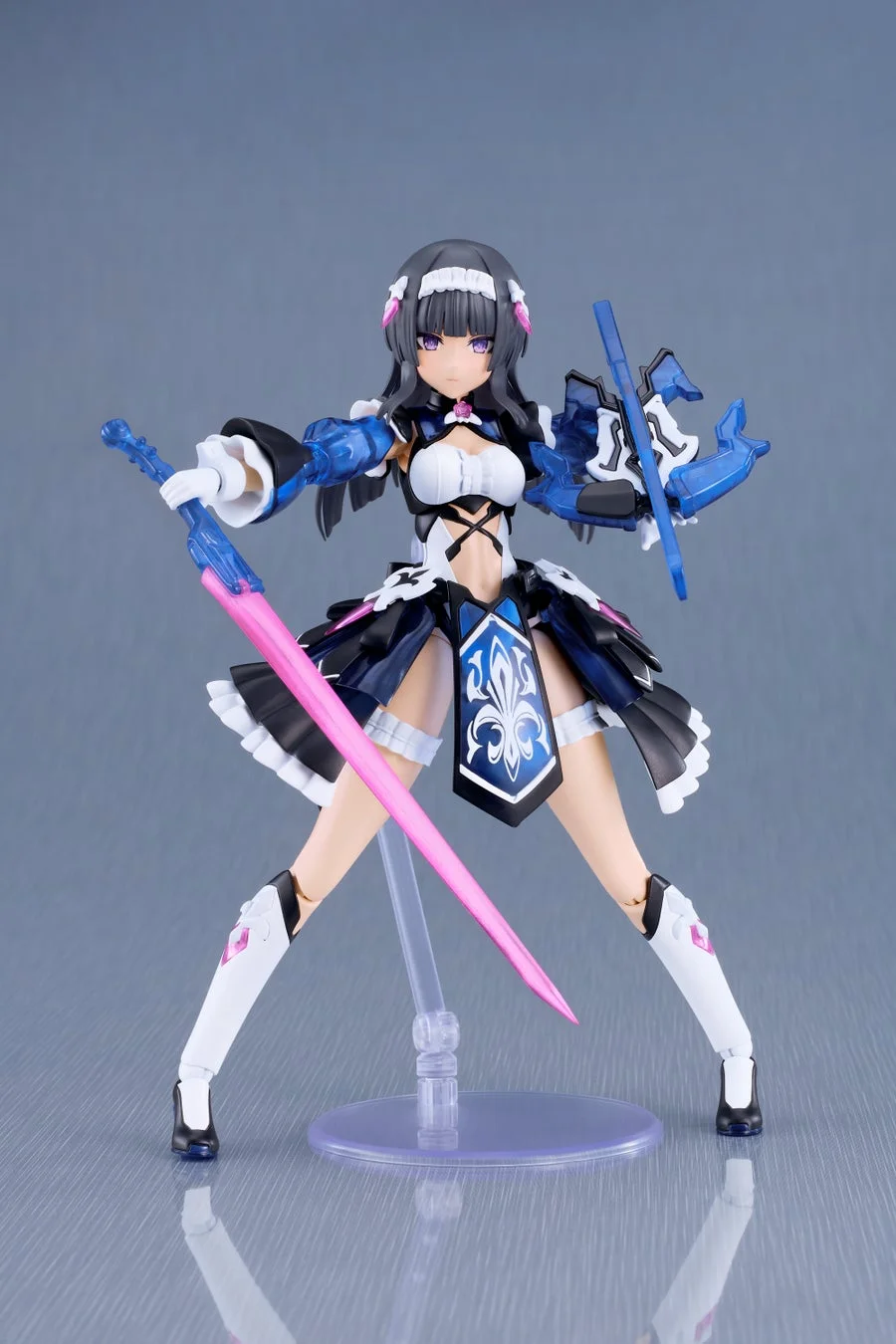 黒髪と紫の瞳を持つ美少女アクションフィギュアが、黒、白、青を基調とした衣装を身につけ、ピンクの剣と青い武器を構えてポーズをとっている。
