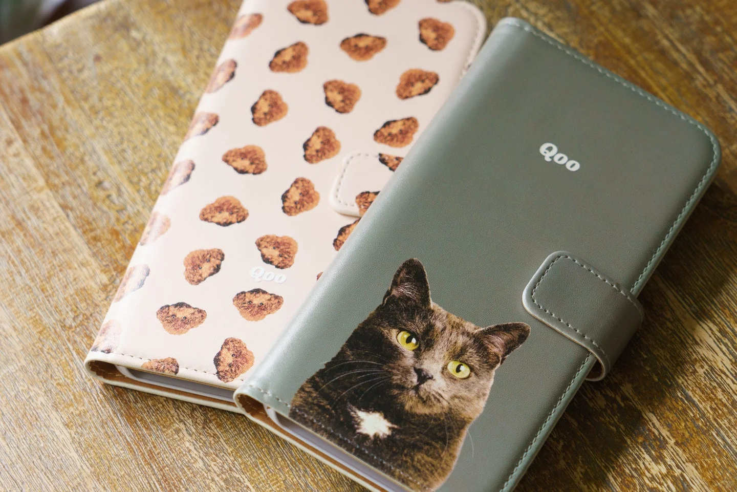 猫の顔がデザインされた手帳型スマホケースと、小さな柄が散りばめられた淡いピンクのケース