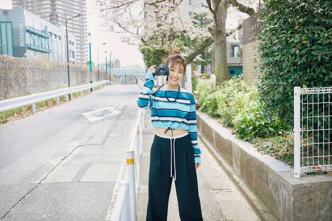 桜が咲く街路でカメラを構える鷲見玲奈さん