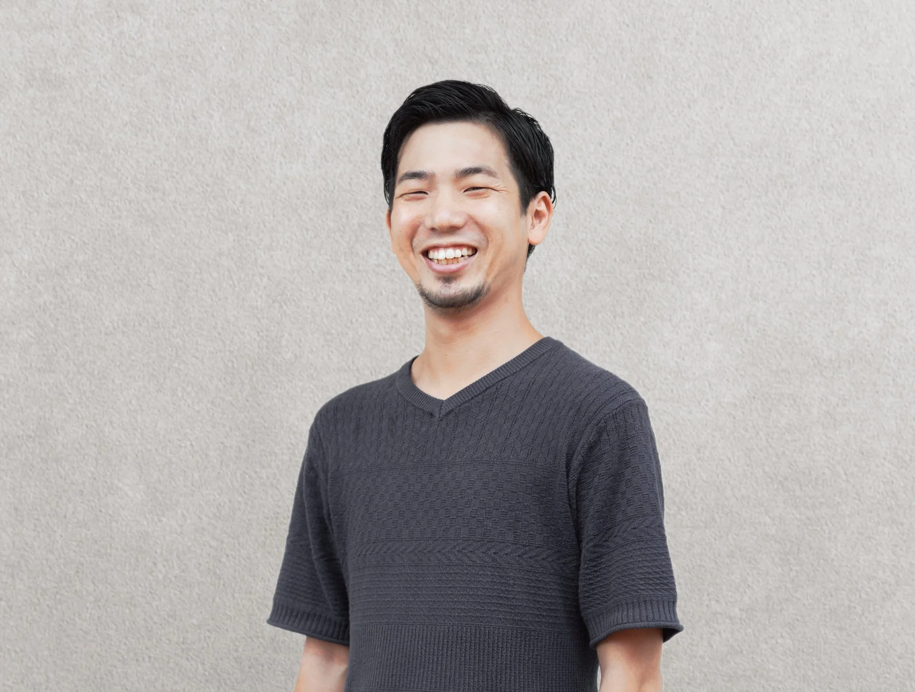 明るい灰色の壁を背景に、グレーのVネックTシャツを着たアジア人男性