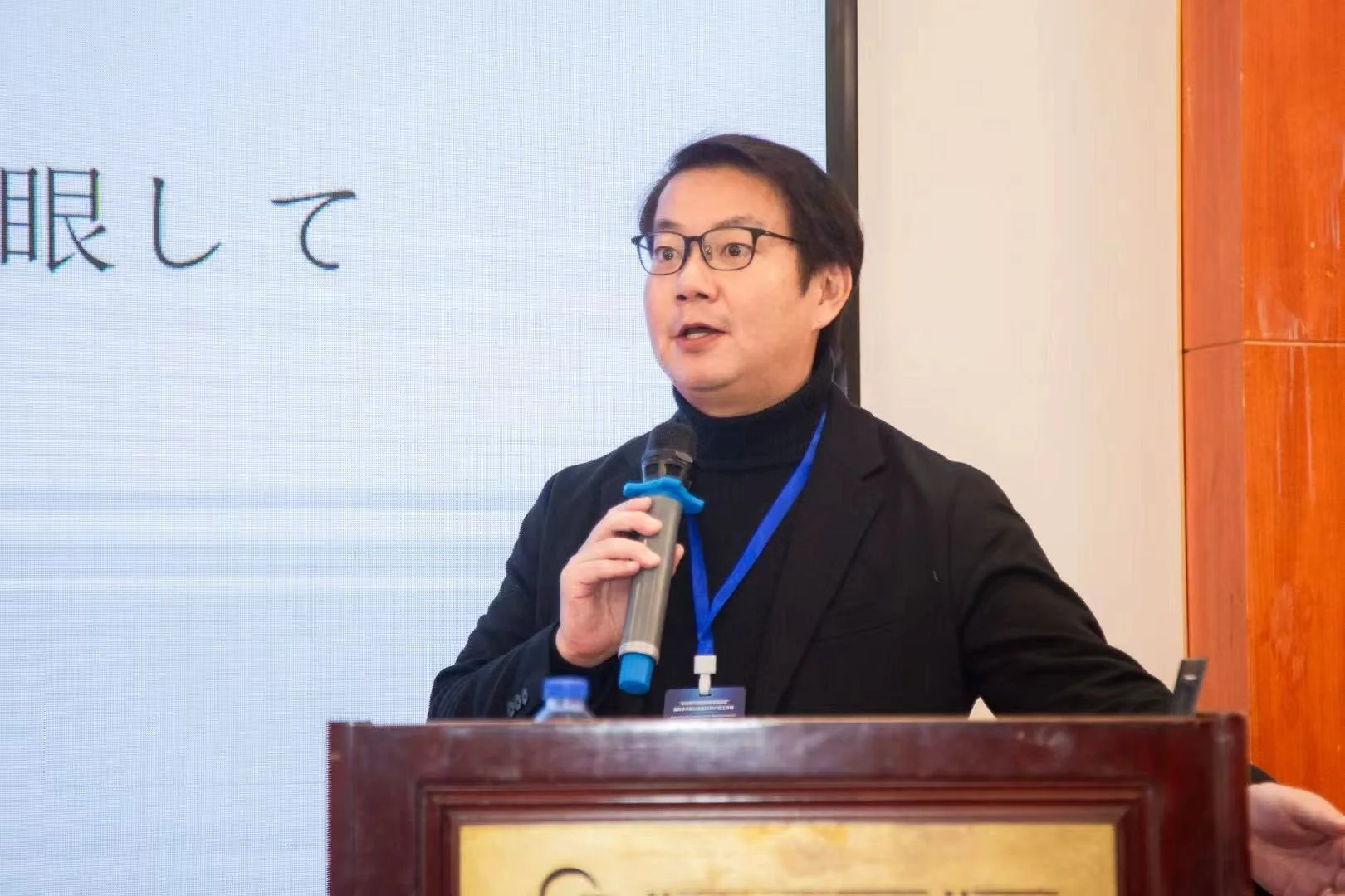 眼鏡をかけた男性がマイクを手に講演を行っている様子