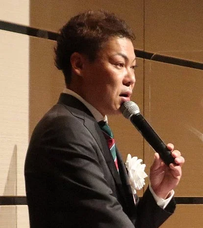 スーツを着用した男性がマイクを持って話している様子