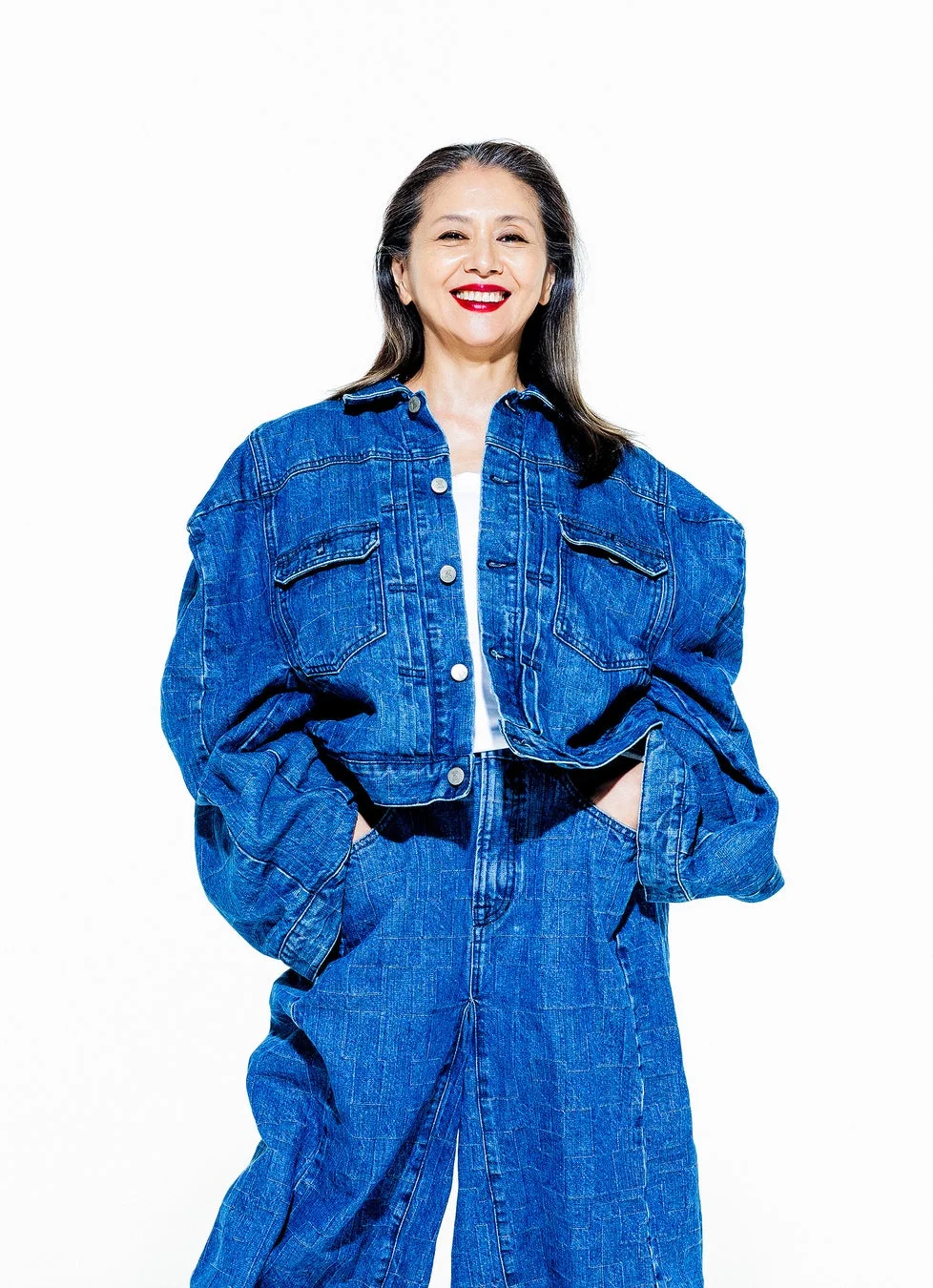 オーバーサイズのデニムジャケットとワイドレッグジーンズを着用し、笑顔でポーズをとる女性