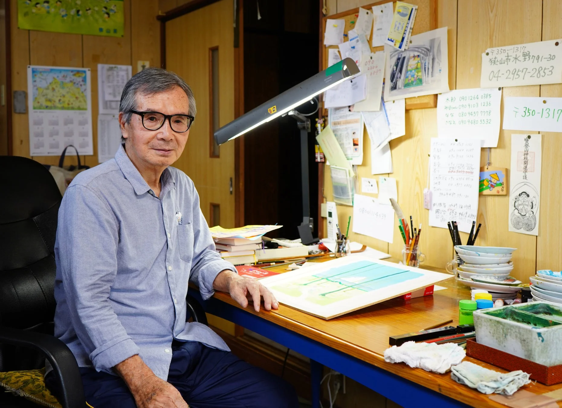 眼鏡をかけた高齢の男性がアトリエで絵画制作に集中する様子