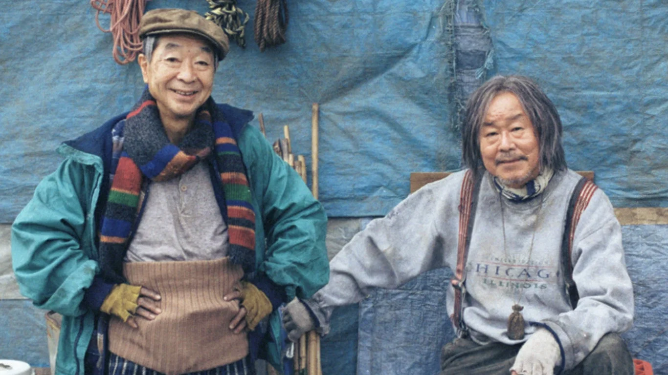 青いシートを背景に、笑顔の高齢男性二人が写っている