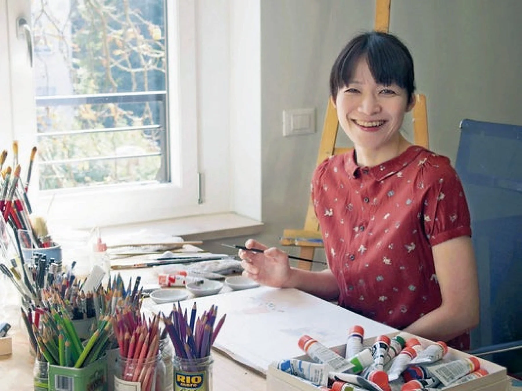 アトリエで絵筆を持つ笑顔の刀根里衣氏