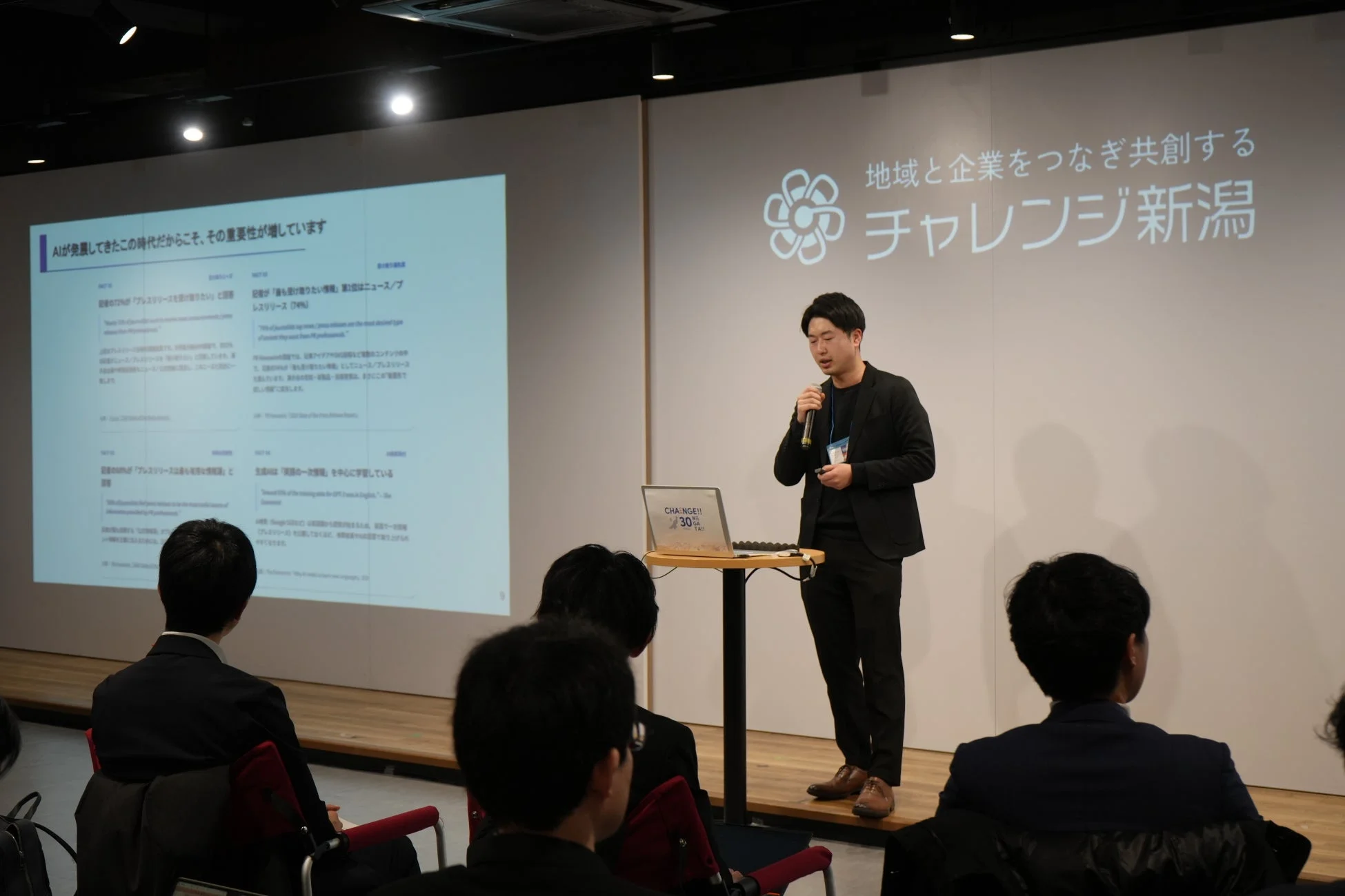 講演者がステージでマイクを持ち、AIとプレスリリースの重要性についてプレゼンテーション