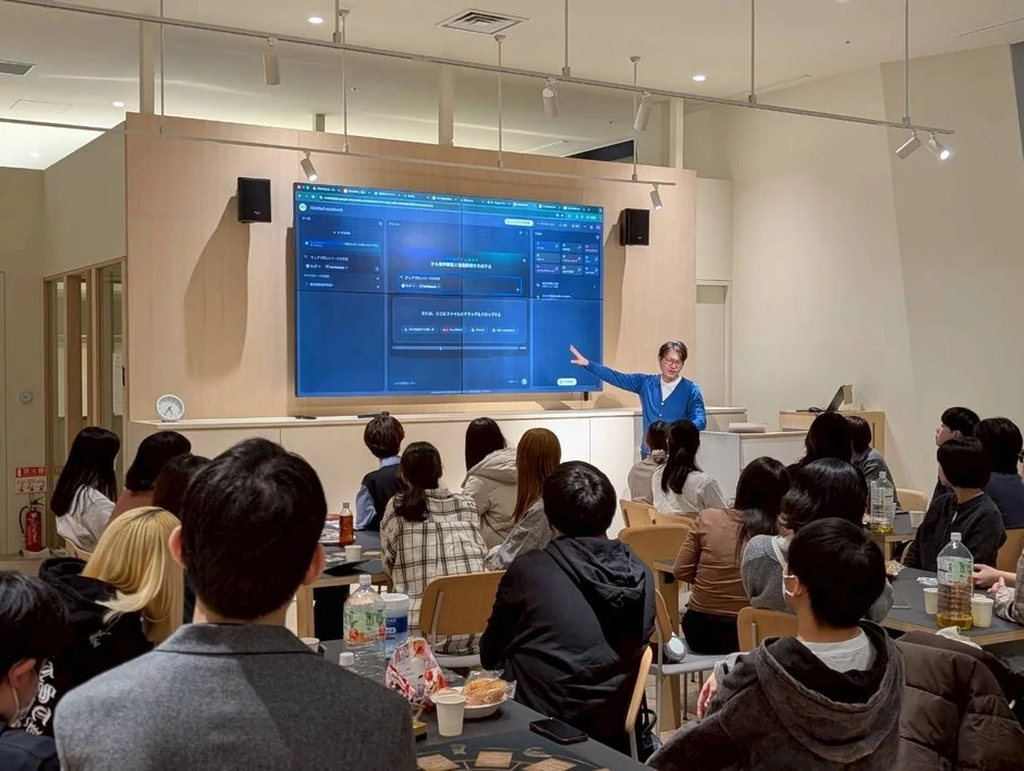 明るい会議室で、一人の男性が大画面に表示されたソフトウェアについて聴衆に説明しています