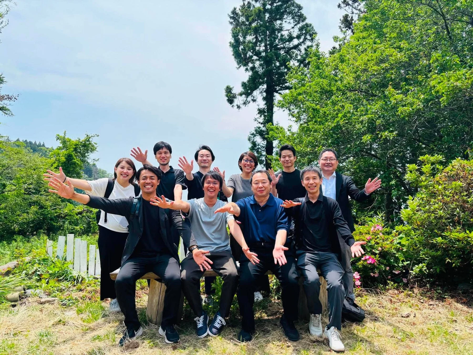 屋外で笑顔の9人がポーズをとっている集合写真