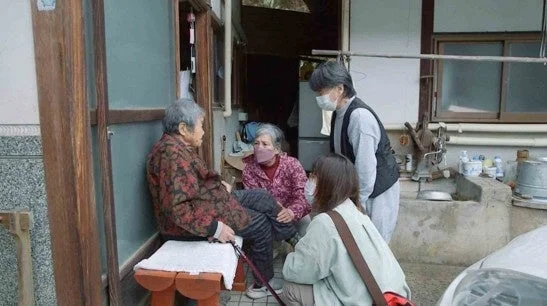日本家屋の玄関先で談笑する哲代さんと人々