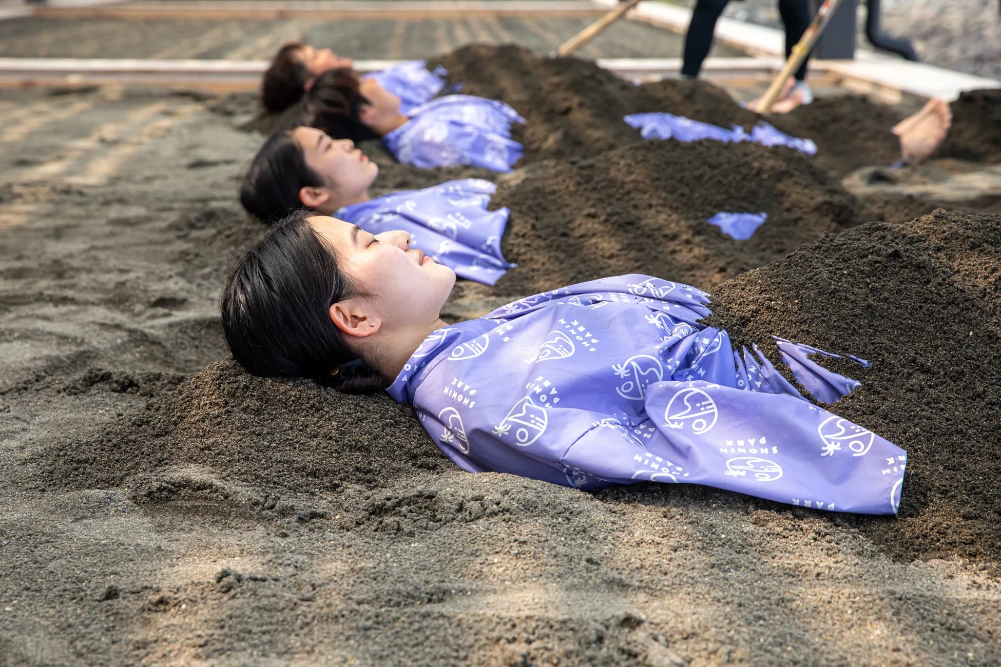 紫色の着物を着て砂風呂を楽しむ人々の様子