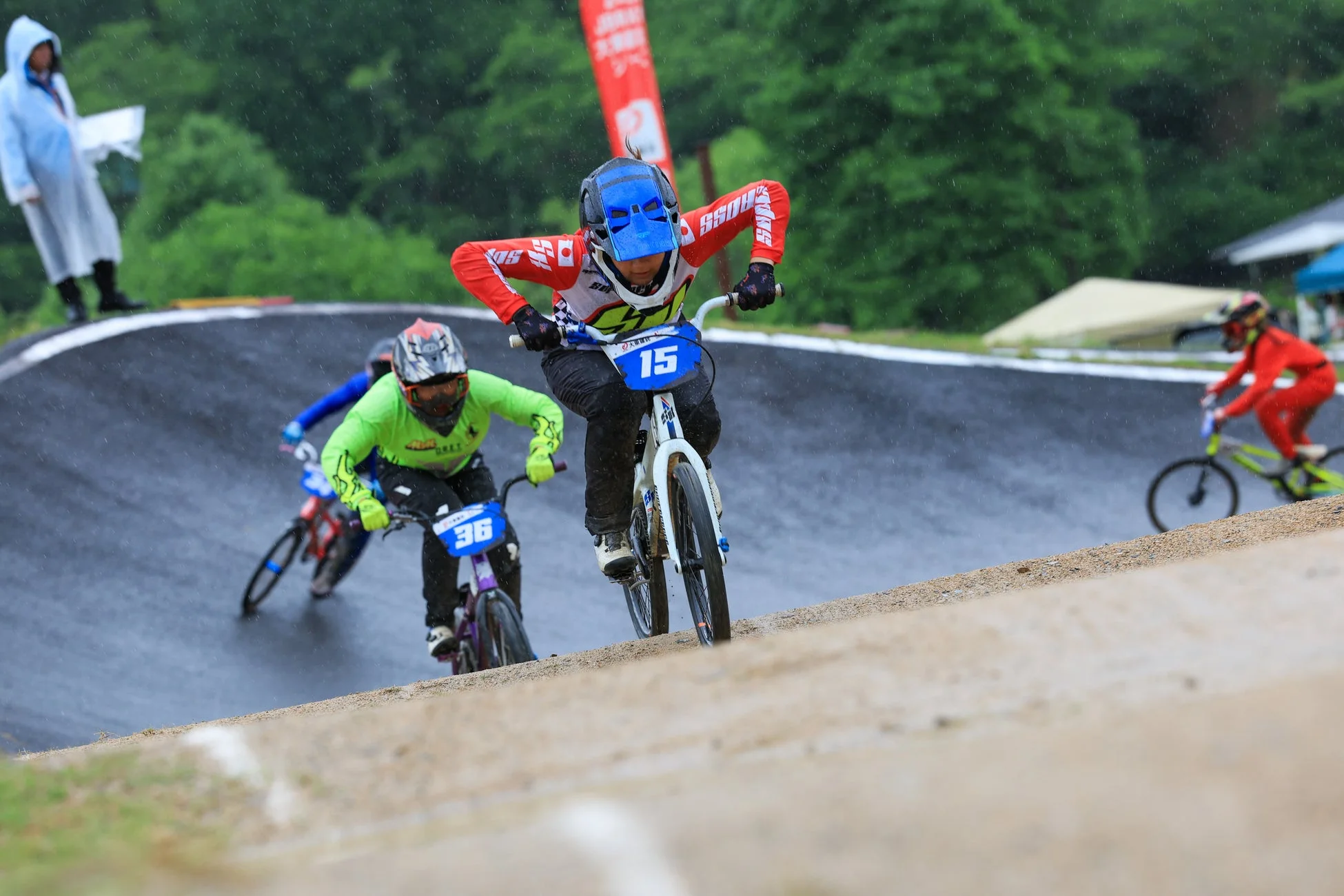 雨降るBMXレースで、ライダーたちが泥だらけのトラックを疾走