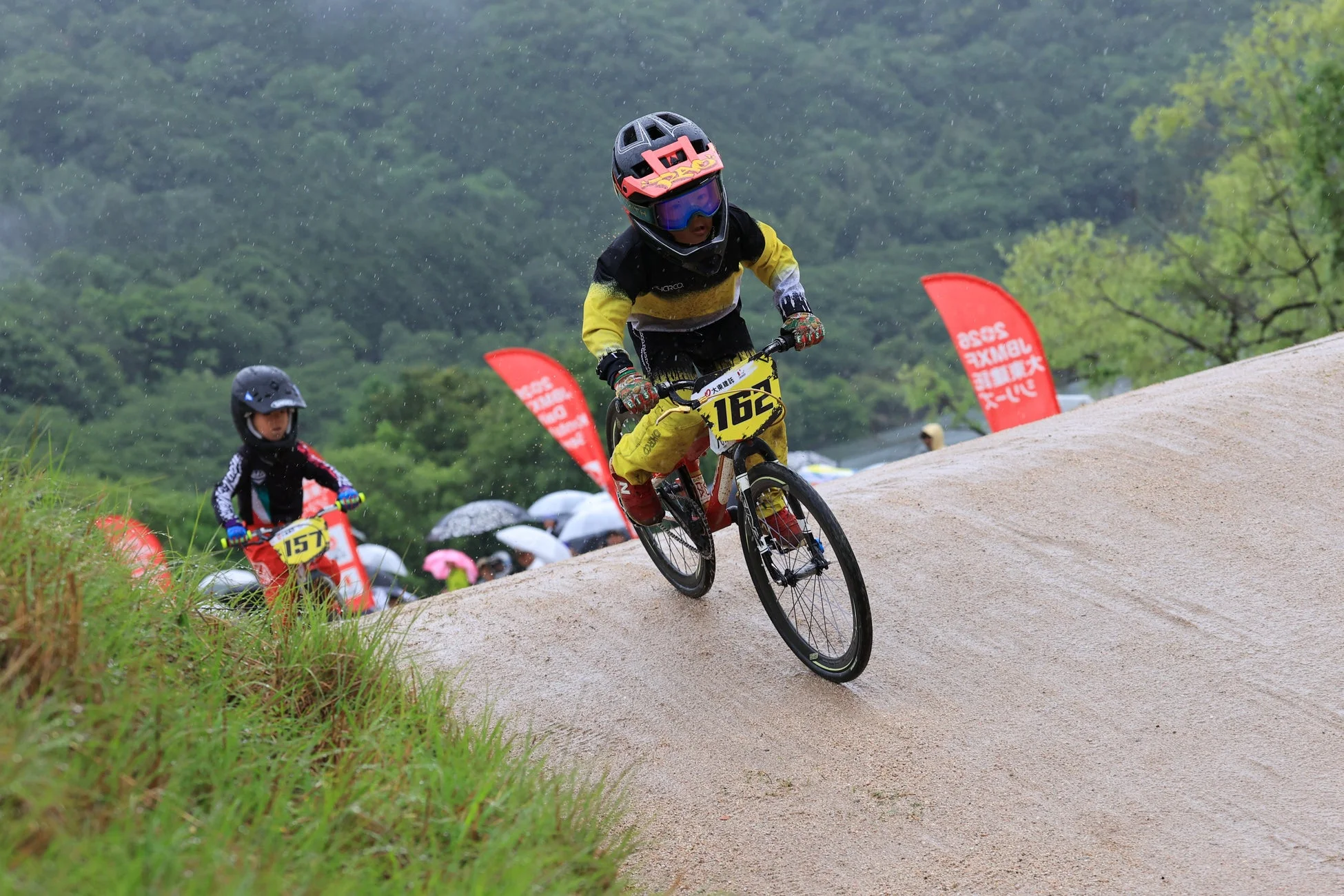 雨が降る中、子供たちがBMXレースでダートトラックを走る