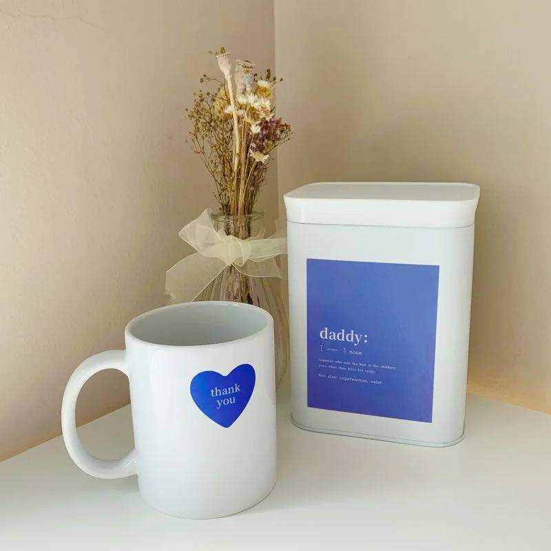 白いマグカップに青いハートと「thank you」の文字が描かれ、隣には「daddy」の定義が書かれた白い容器が置かれている