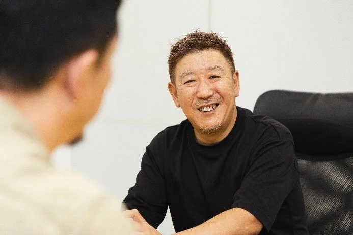 笑顔で話す男性と、その話を聞くもう一人の人物が写っています