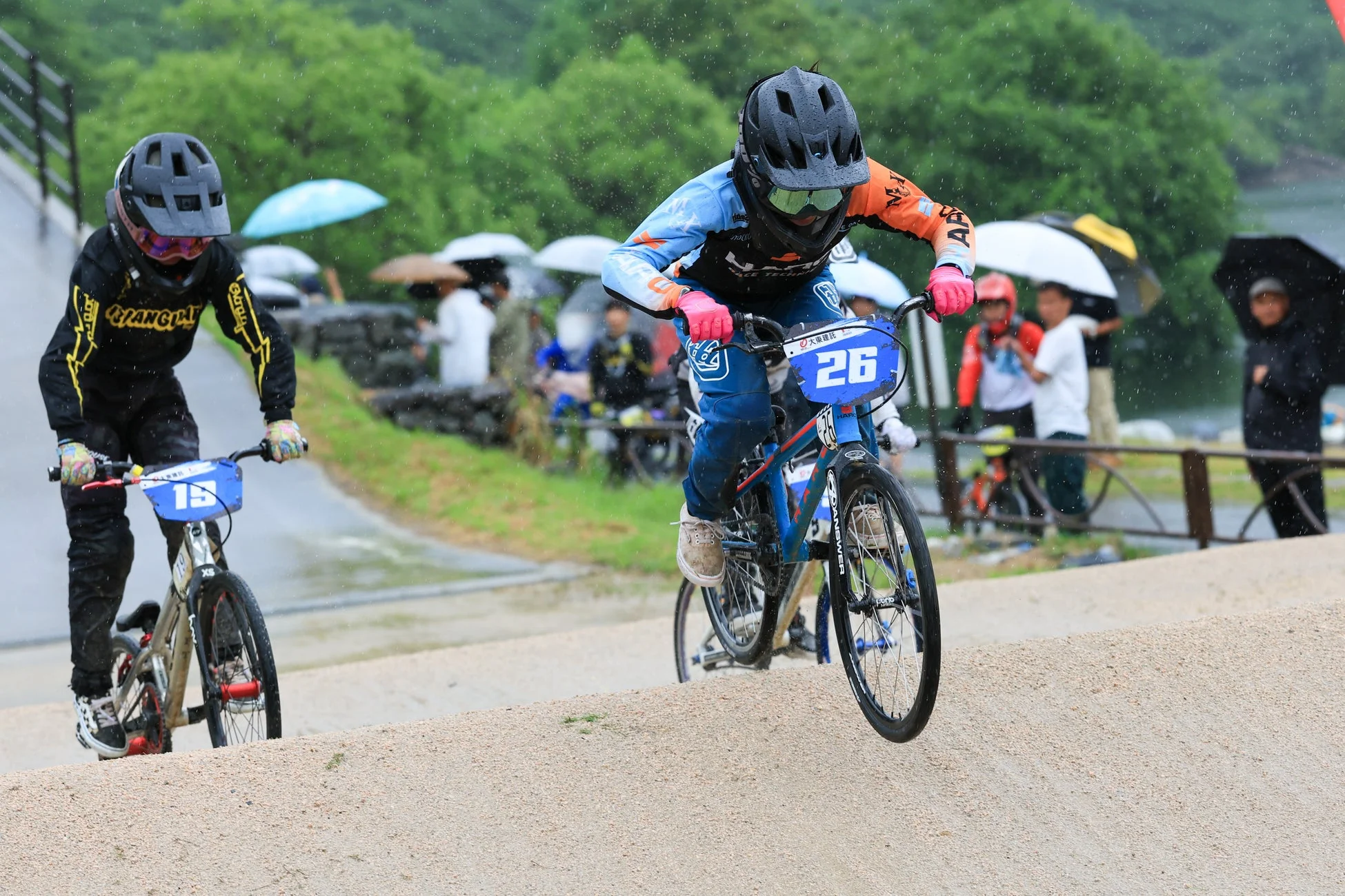 雨が降る中、BMXレースに参加する2人のライダーがダートコースを走行