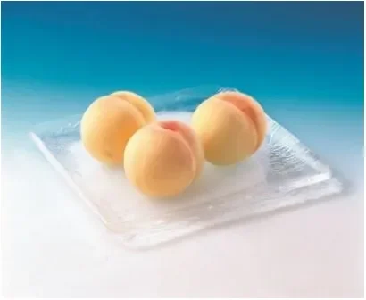 透明なガラスの皿に、皮をむいた状態の瑞々しい桃が3つ並べられています。青と白のグラデーションの背景が、涼しげな夏の雰囲気を醸し出しています。