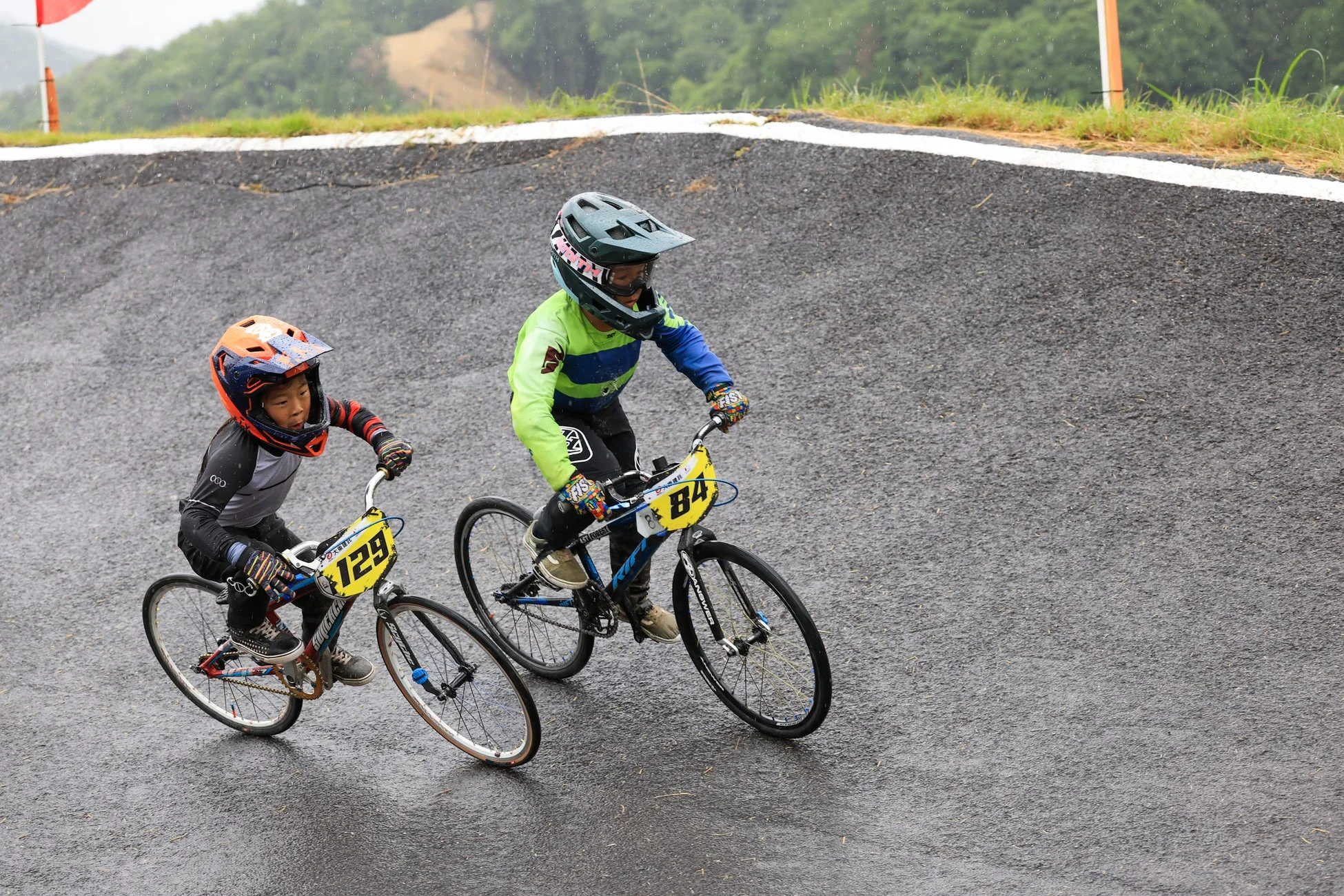 雨のBMXトラックで、真剣な表情で自転車を漕ぐ二人の子供レーサー