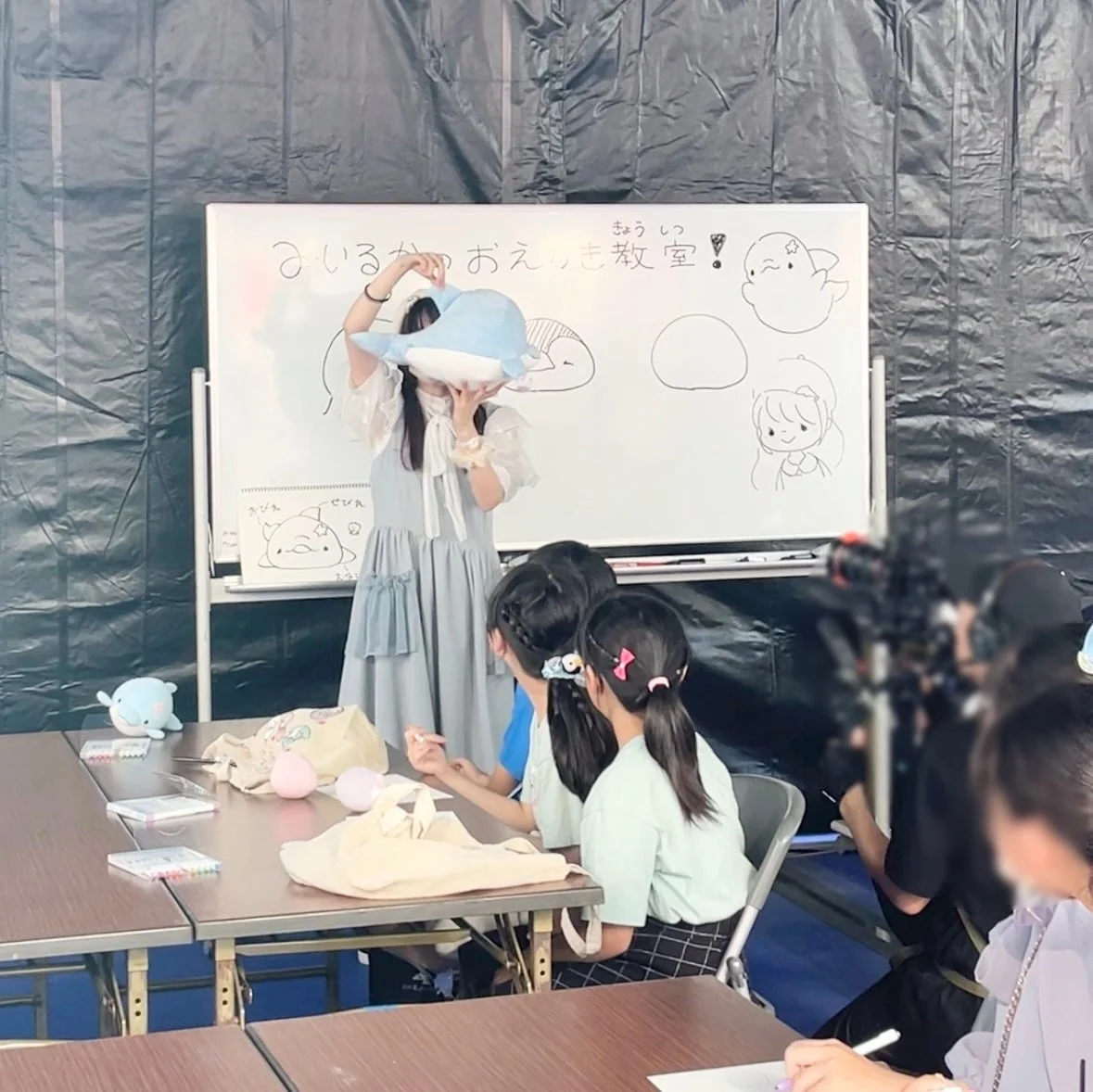 イルカのぬいぐるみを使って子どもたちに絵の描き方を教えている女性