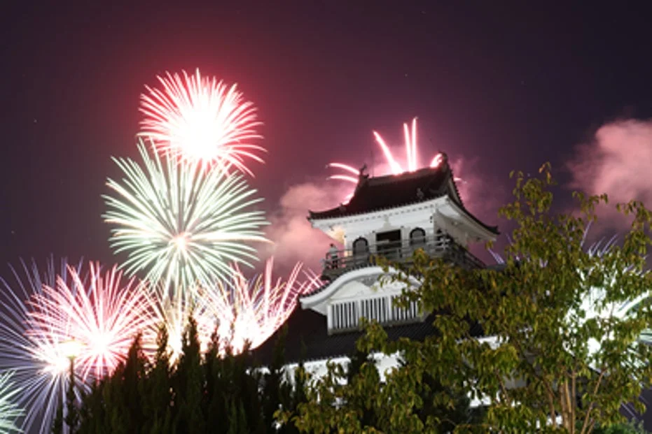 夜空に打ち上げられた色鮮やかな花火が、日本の伝統的な城を背景に美しく輝いています。夏の夜の祭りを思わせる幻想的な風景です。