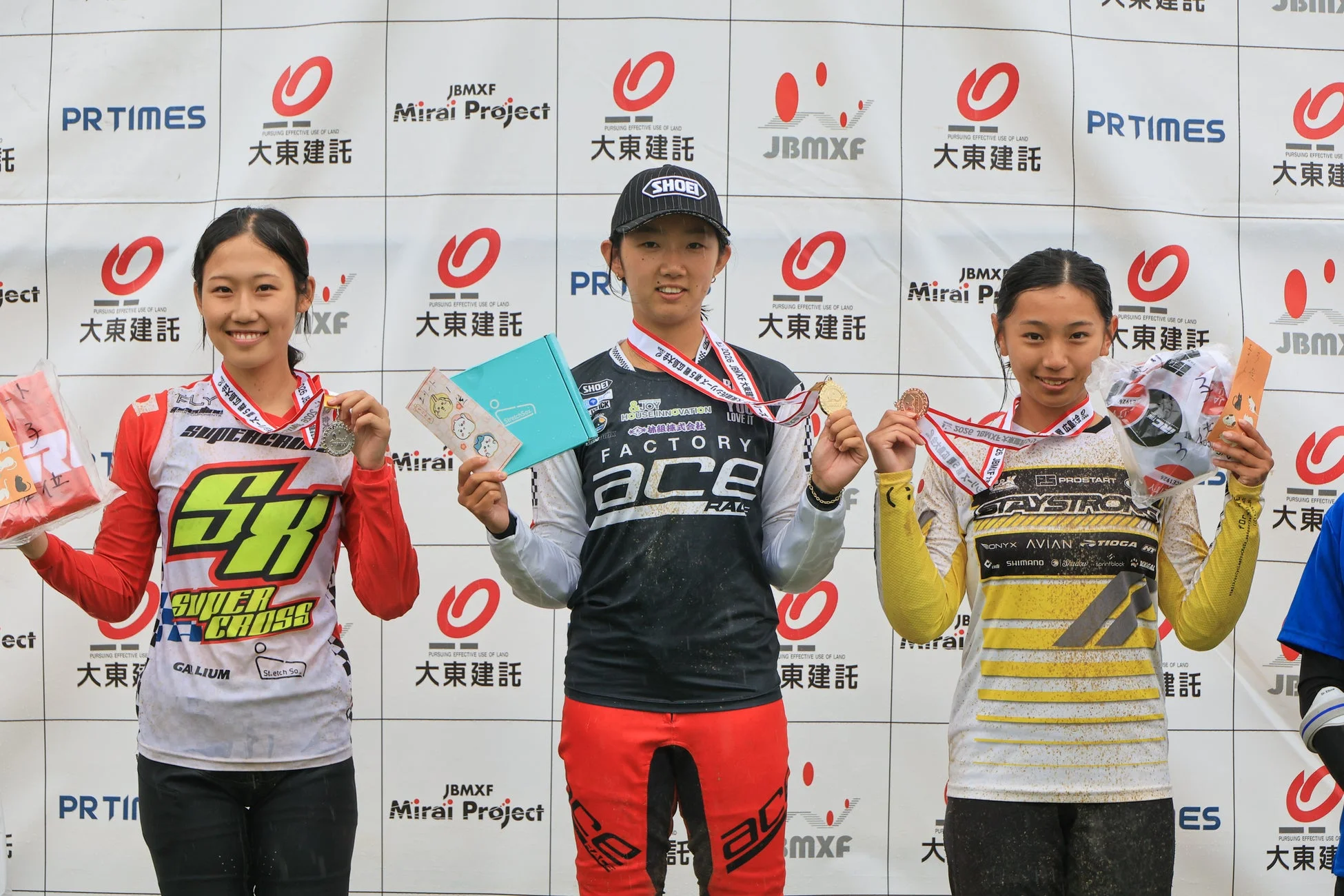 BMX競技の表彰台でメダルと賞品を手に笑顔で並ぶ女性アスリート