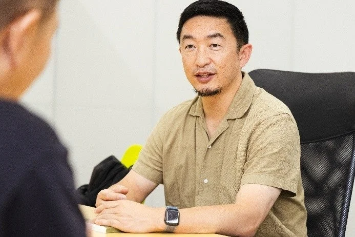 ベージュのシャツを着た男性が誰かと対話している様子