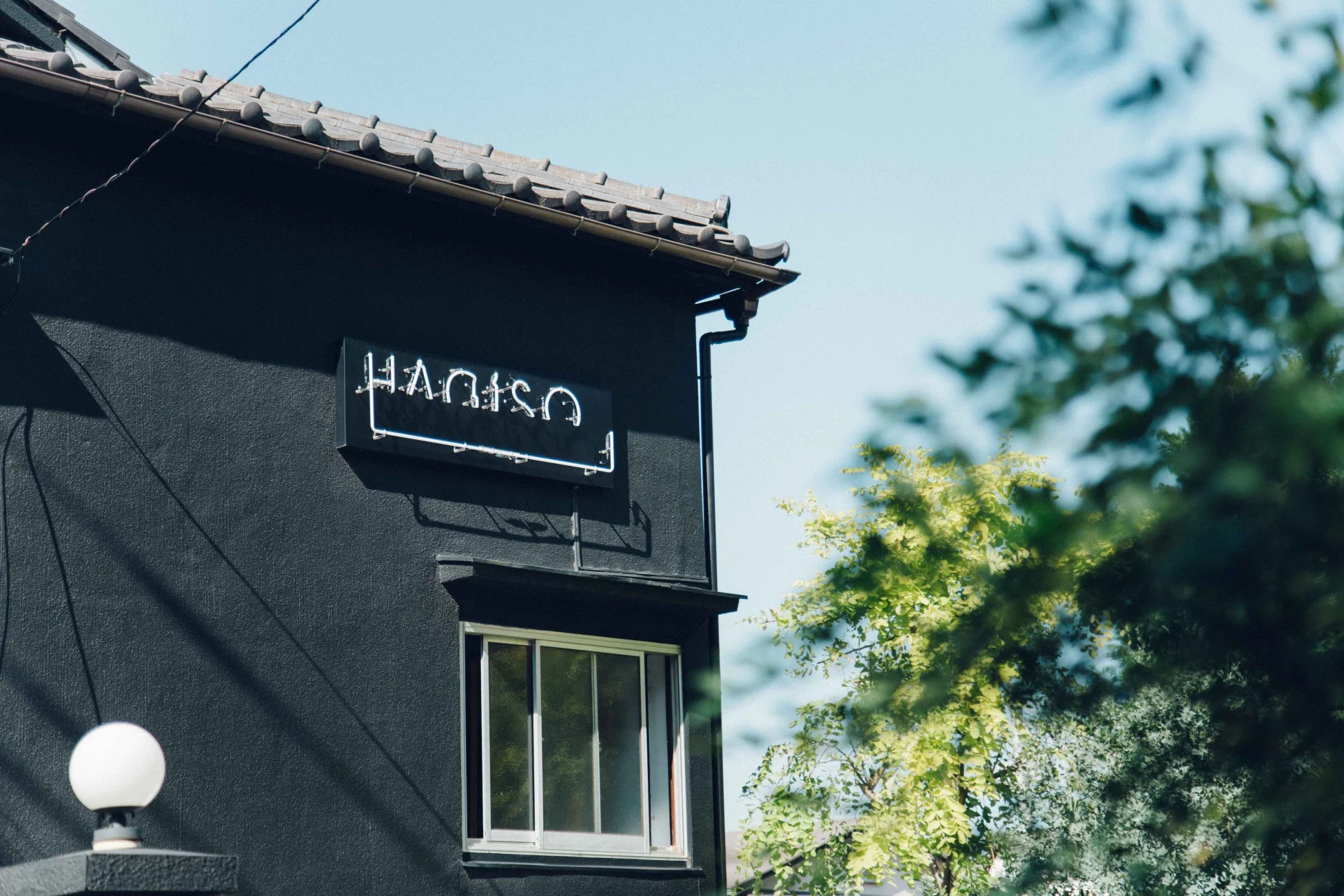 黒い壁の建物の一部が写っており、伝統的な瓦屋根と「HANTSU」と書かれたネオンサインが特徴的です