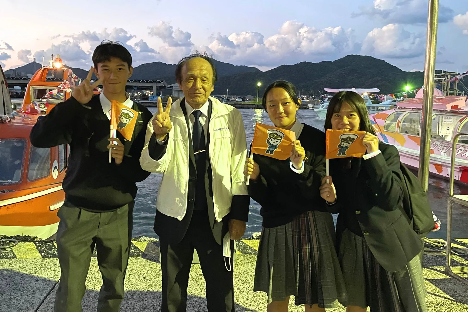 夕暮れの港で記念撮影をする学生たち