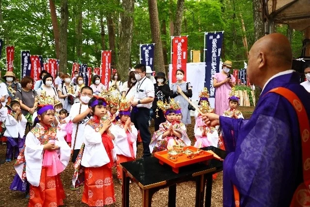 森の中で、伝統的な衣装を身につけた子供たちが僧侶の指導のもと、大人たちに見守られながら厳かな儀式に参加している