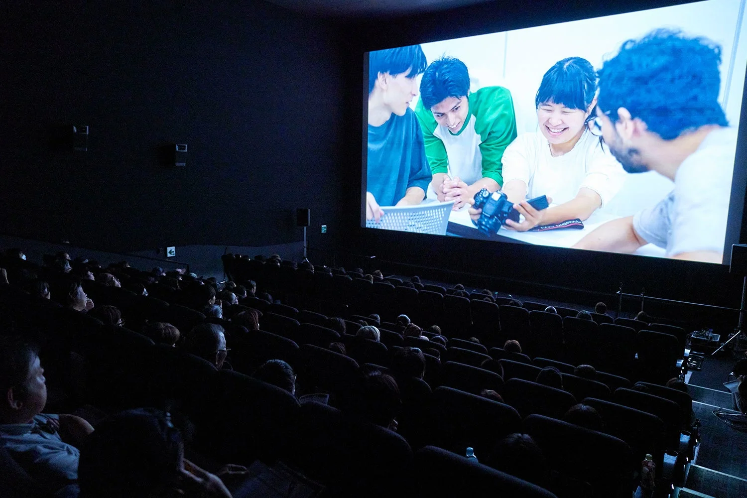 暗い映画館で多くの観客が大きなスクリーンを見上げている様子