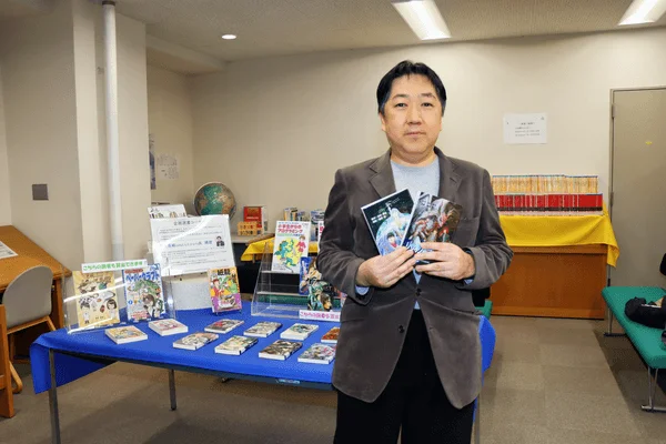 企画展コーナーで本を持つ米村貴裕氏