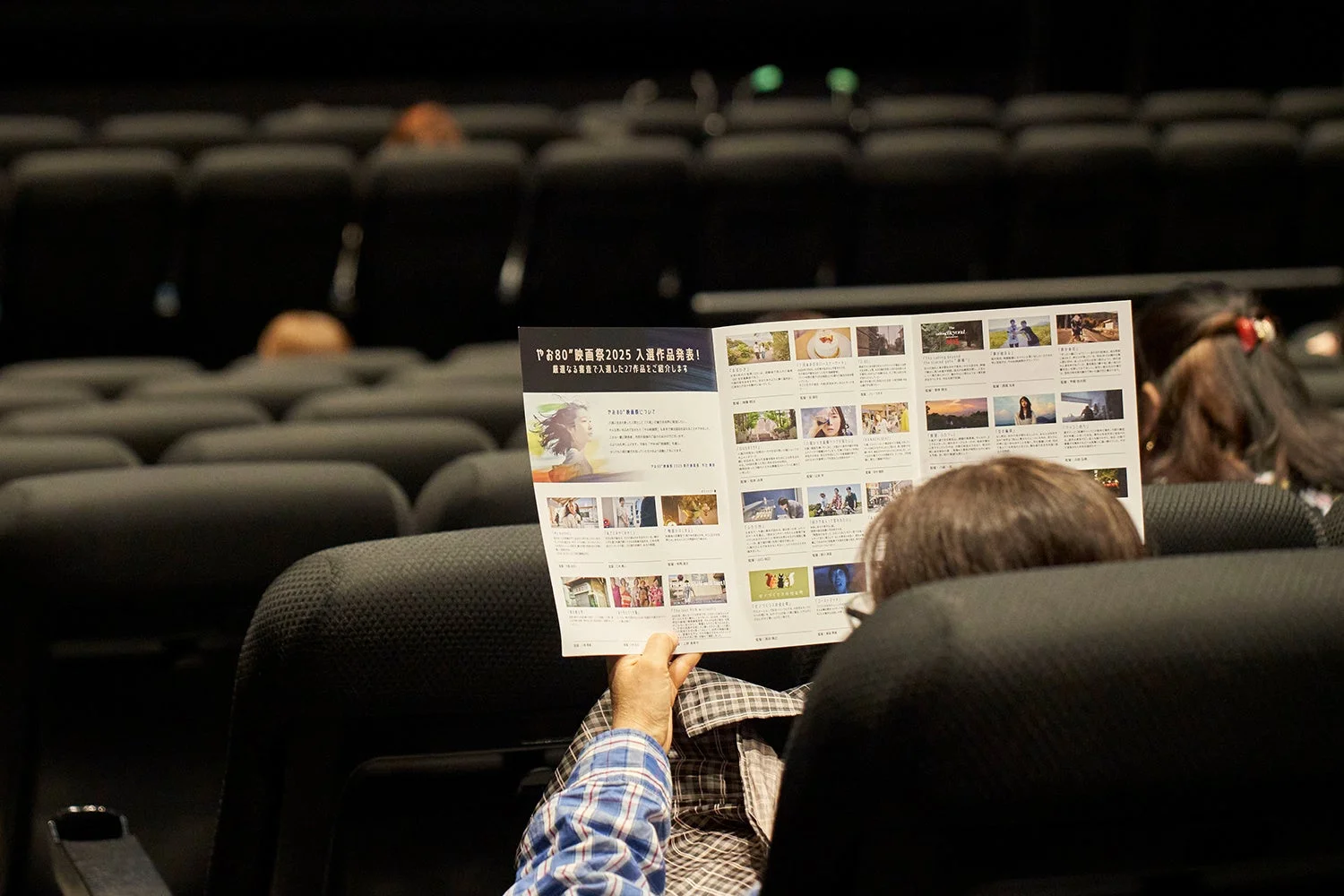 暗い会場の座席で、一人の人物が映画祭のパンフレットを読んでいる様子