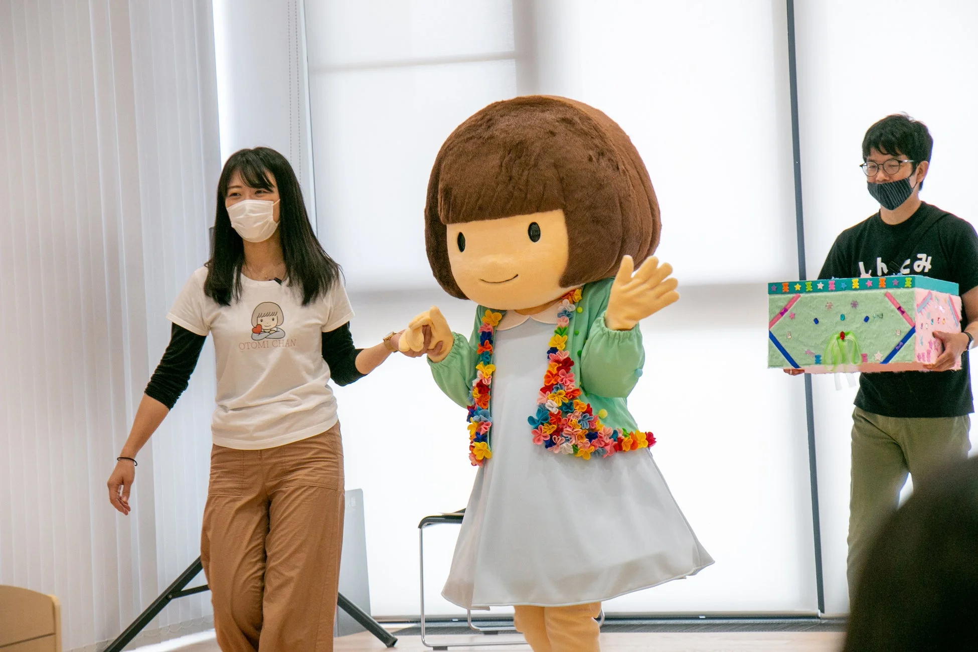 花飾りのついた衣装を着た大きなゆるキャラと手をつなぐ女性