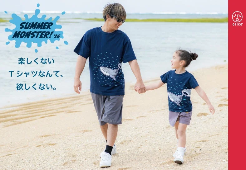 ビーチで手をつないで歩く親子が、お揃いのジンベエザメ柄Tシャツを着て笑顔を見せています。