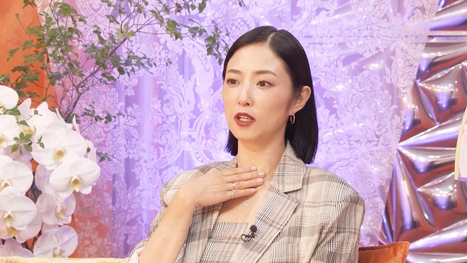 ショートヘアの女性がスタジオらしき場所で話しており、チェック柄のジャケットを着用