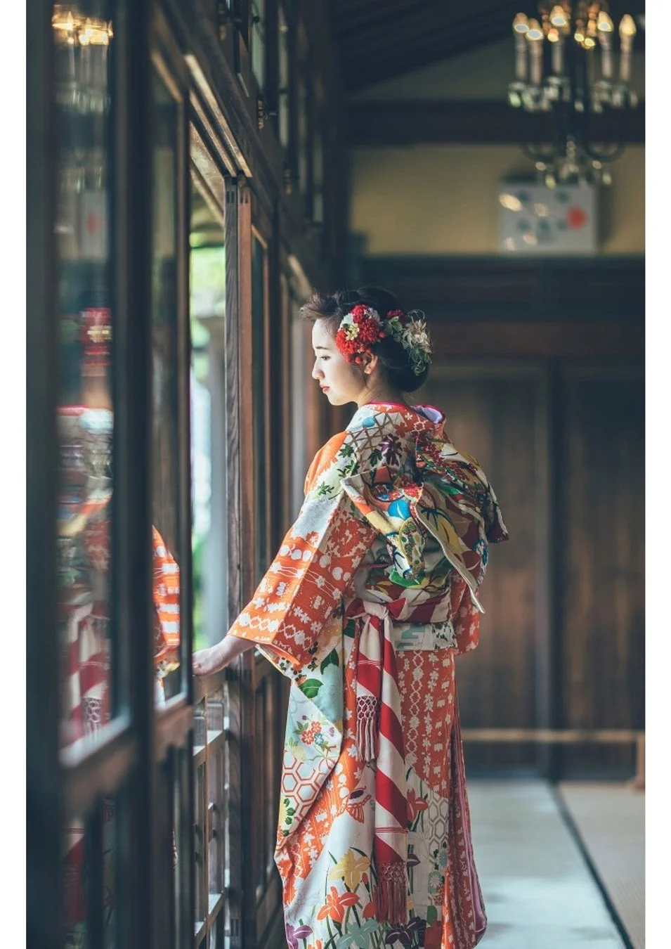 華やかな着物を着た女性が、伝統的な日本家屋の窓辺に立ち、外を眺めている