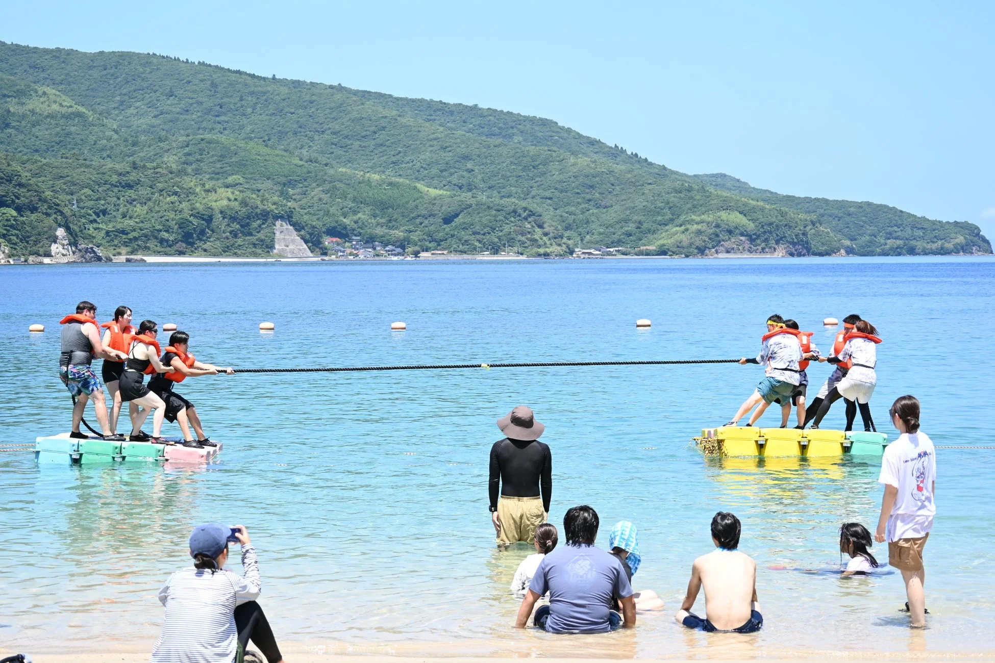 夏の海でライフジャケットを着て綱引きを楽しむ人々