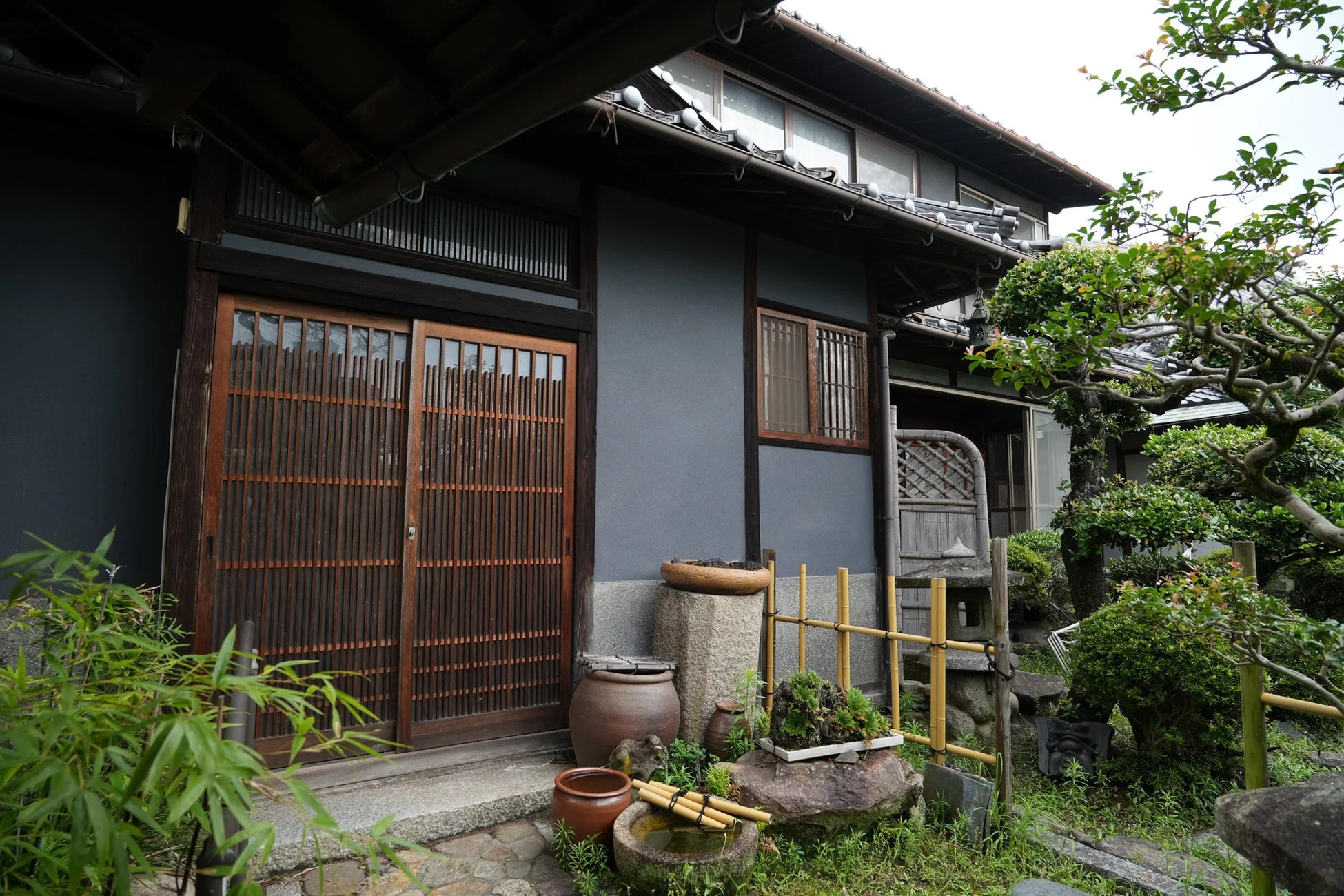 瓦屋根と木製の引き戸が特徴的な伝統的な日本家屋と、手入れされた庭園が写っています。