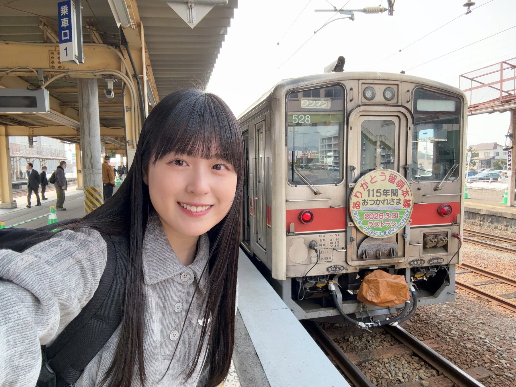 駅のホームで笑顔の女性が列車とセルフィーを撮っている