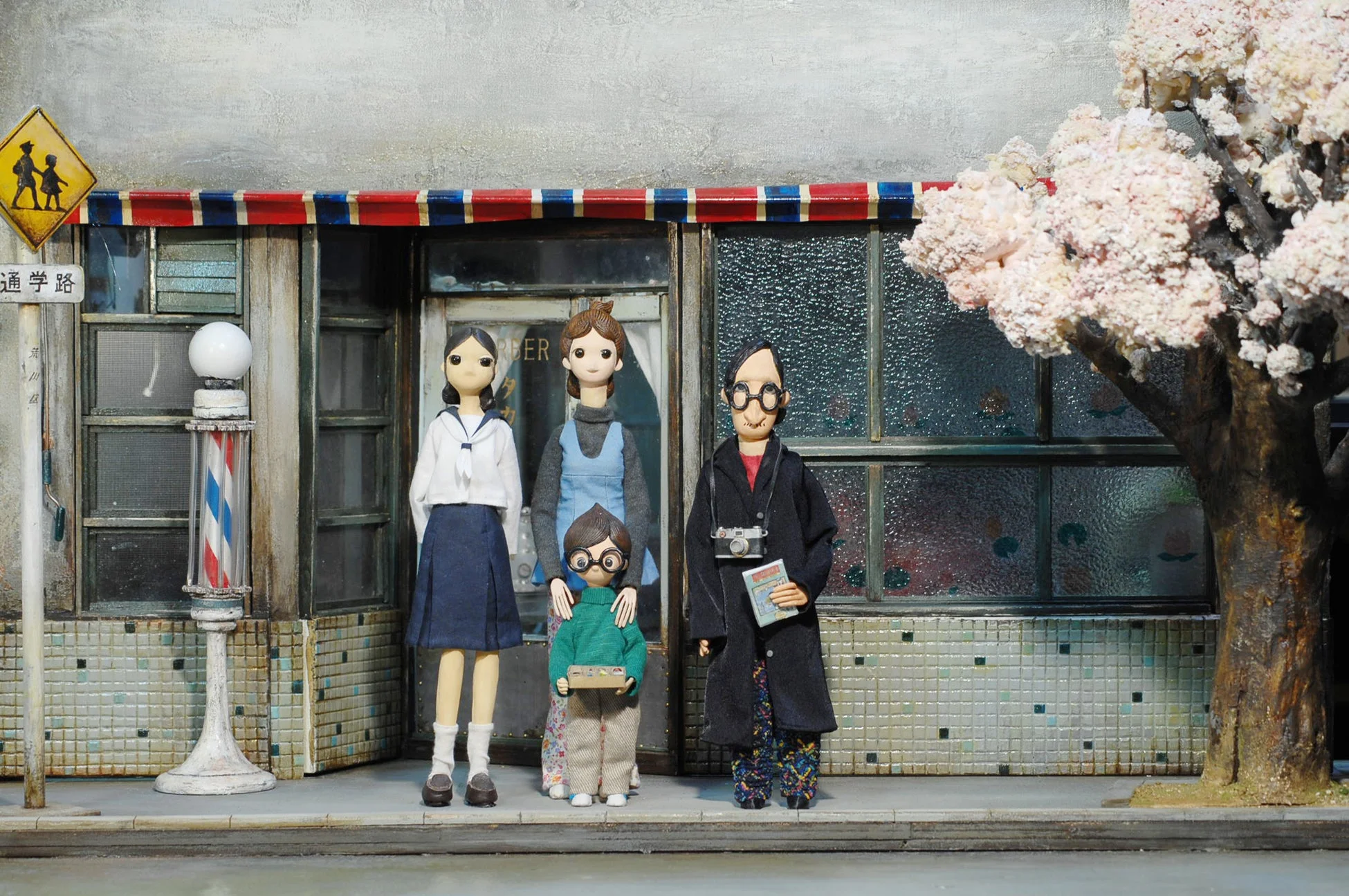 クレイアニメのような人形の家族4人が、理髪店らしき古い商店の前で立っている情景