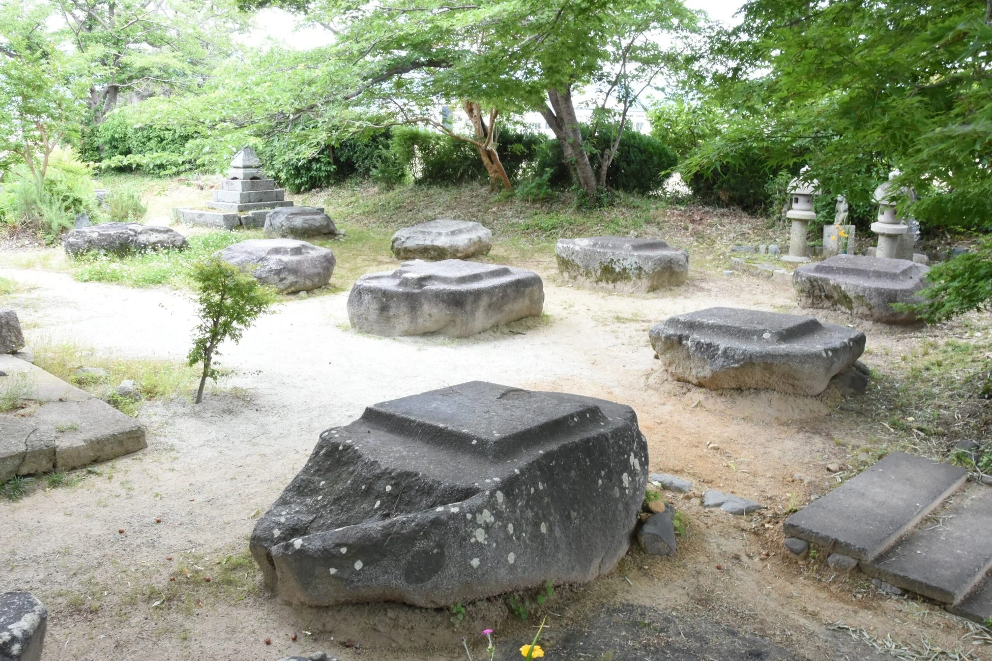 古い石の基礎や石碑が点在する、緑豊かな庭園の風景