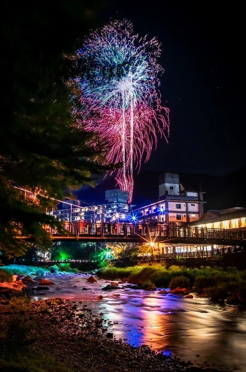 夜空に咲く色鮮やかな花火が川面に映り込み、幻想的な夜景を創り出しています