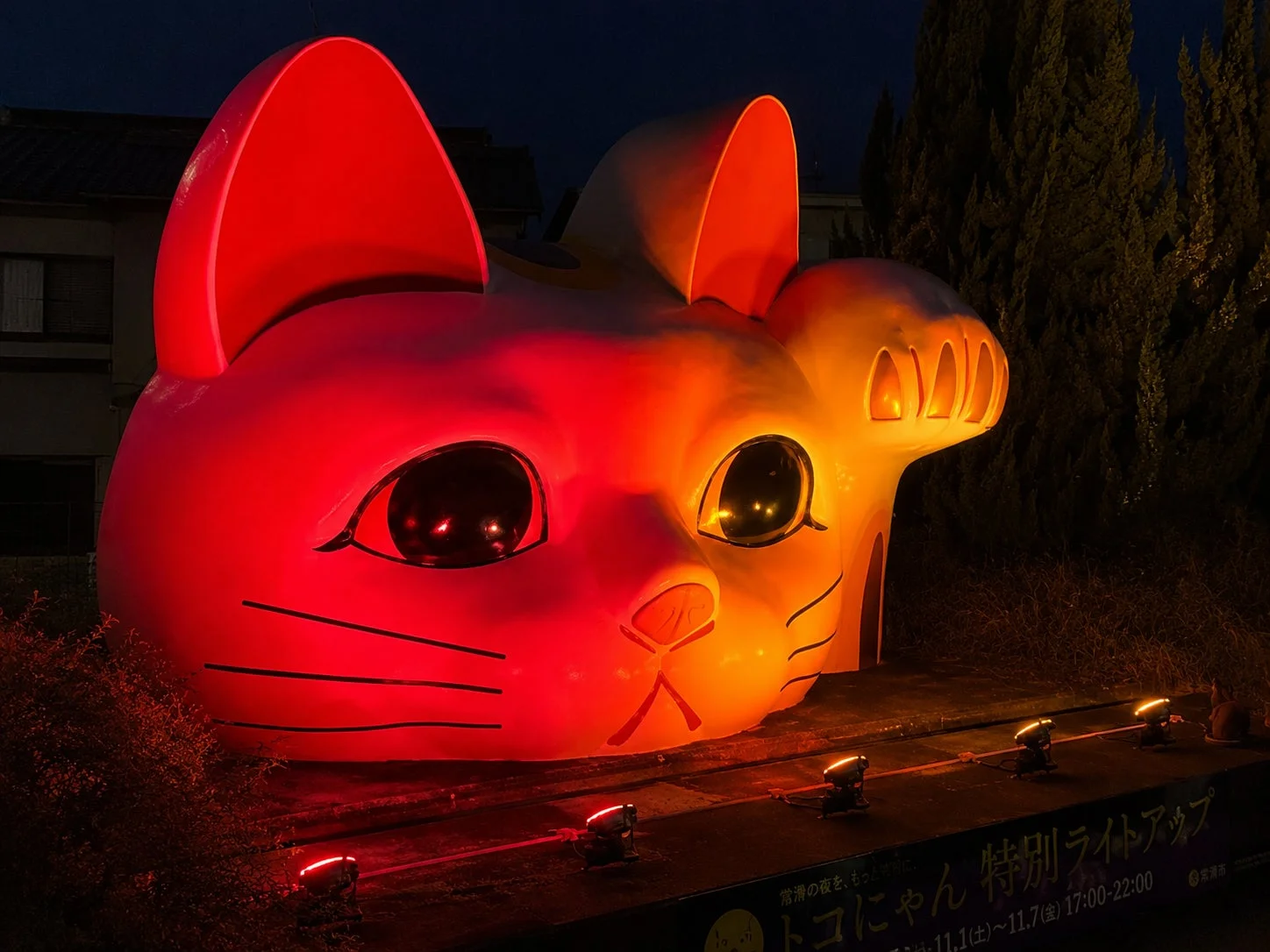 常滑市のシンボルである巨大な招き猫「トコにゃん」が、赤とオレンジ色に鮮やかにライトアップされた夜の様子