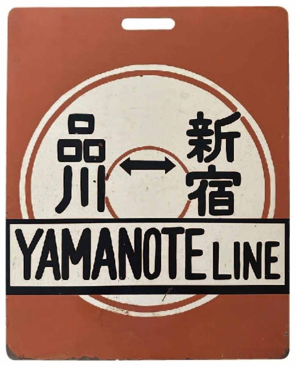山手線の駅名である品川と新宿が両方向矢印で示され、「YAMANOTE LINE」と英語で書かれたレトロな案内板